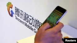 在北京举行的全球移动互联网会议上一名参观者在腾讯展台前玩智能手机上的游戏。(2015年4月28日)