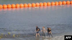 资料照片:移民们在德克萨斯州边境格兰德河边沿着一串橙色浮标行走。(2023年7月17日)