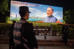 2018年12月17日,在中国深圳,保安人员站在中国已故最高领导人邓小平的宣传牌前面,牌子上写着“坚持党的基本路线一百年不动摇”。