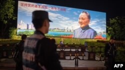 2018年12月17日,在中国深圳,保安人员站在中国已故最高领导人邓小平的宣传牌前面,牌子上写着“坚持党的基本路线一百年不动摇”。