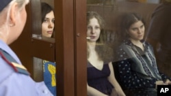 2012年8月8日俄罗斯女庞克摇滚乐队Pussy Riot的成员歌手托洛尼克娃(图左), 奥尔约其纳(图中),和萨姆泽维奇(图右)坐在俄罗斯一个法庭的一个拘禁她们的玻璃隔离的角落