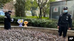 一名男子在武汉中心医院为李文亮逝世一周年献花的纪念地驻足,一名警察站在一旁。(2021年2月6日)