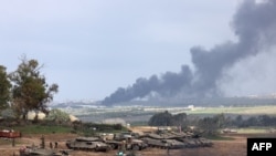 2024年1月14日,以色列和哈马斯的战争进入第100天,在以色列与加沙地带的边境地带,以色列士兵站在坦克旁边。以色列的炮击使加沙地带浓烟滚滚。(法新社)