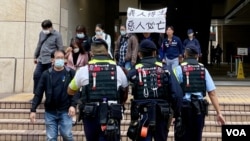 2024年11月19日,香港民主派初选案被告吕智恒的养母Elsa在吕智恒被判刑后,在西九龙裁判法院大楼外高举”义人得生、恶人必亡”的标语。她立即被多名香港警员包围及带上警车。 (美国之音照片)