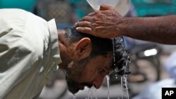Seorang relawan menuangkan air untuk menyejukkan seorang pria di tengah hari yang panas di Karachi, Pakistan, 21 Mei 2024. (Foto AP/Fareed Khan)