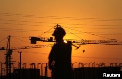 在夕阳映照下,一名建筑工人扛着锤子走在江苏南通某居民楼建筑工地。(2013年8月6日)