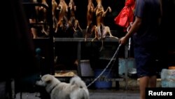 资料照:广西玉林市一名牵着宠物犬的人路过卖狗肉的摊子。(2018年6月21日)