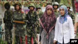 资料照:在新疆乌鲁木齐市的两名维吾尔族妇女步行经过中国武警队伍。