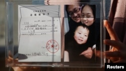 资料照:中国维权律师王全璋的妻子李文足手举全家福照片和天津警方的逮捕通知书。(2018年12月17日)