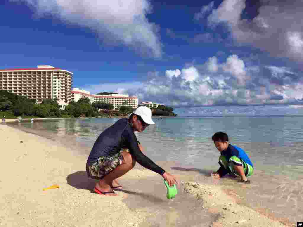 关岛海滨风光如画,碧水金沙。居民仁川健司与他的儿子秀树在关岛的海滩玩耍(2017年8月14日)。仁川健司知道朝鲜的威胁,但不怎么担心。他说,朝鲜的导弹会落在水里,而不是关岛。 