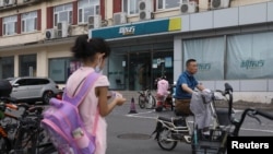 一个女孩站在北京街头一个新东方校外补习学校的附近。(2021年7月26日)