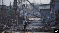 Một người đi qua con đường với những tòa nhà bị hư hại ở Wajima thuộc bán đảo Noto, hướng ra Biển Nhật Bản, phía tây bắc Tokyo, ngày 6 tháng 1 năm 2024, sau trận động đất chết người hôm thứ Hai.