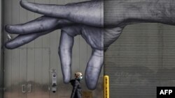 一位女士戴着口罩走过纽约市中城一座大楼的巨手壁画。(2020年4月22日)