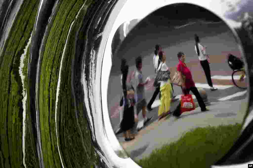 镜中人。在北京一座商业建筑外，一座雕塑中有一轮明镜，镜面上有行人和植物的影像（2017年8月16日）