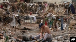 资料照片:洪灾过后,一名男子在北京郊区的小溪里洗衣服。他身后是一片狼藉。(2023年8月4日)