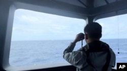 在印尼海事安全局(BAKAMLA)发布的这张没有注明日期的照片中,一名印尼,海事安全局人员在南中国海有争议的北纳土纳海域使用望远镜监视一艘中国海警船的动向。(2024年10月24日)