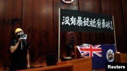 一名进入香港立法会的抗议者站在挂在立法会内的香港殖民地旗帜旁使用扩音喇叭讲话。(2019年7月1日)