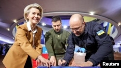 Президентка Єврокомісії Урсула фон дер Ляєн, президент України Володимир Зеленський та прем'єр-міністр Денис Шмигаль підписали український державний прапор перед початком саміту ЄС. Фото: Офіс президента України/REUTERS