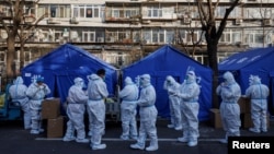 在有新冠病毒阳性民众居家隔离的北京某居民楼外,穿着白色防护服的防疫人员集合,开始他们的执勤班次。(2022年12月8日)