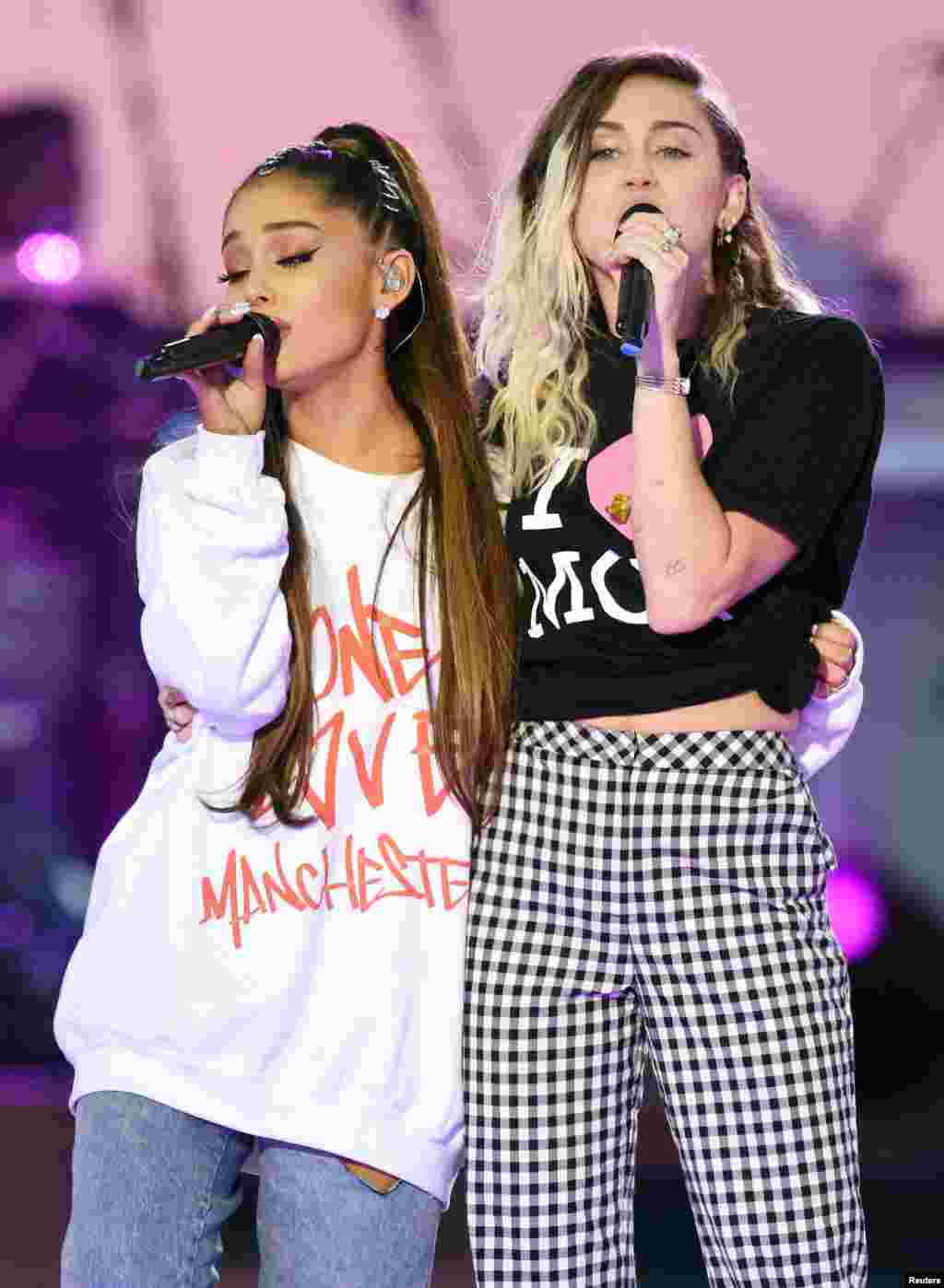 美国流行歌手爱莉安娜·格兰德(Ariana Grande)和歌手、演员麦莉·希拉(Miley Cyrus,右)在曼彻斯特慈善音乐会上演唱(2017年6月4日)。爱莉安娜的衣服上印着“同一个爱·曼彻斯特”。麦莉·希拉曾经主演过美国迪斯尼公司出品的青少年电视情景喜剧《孟汉娜》