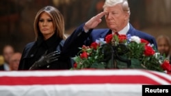 US President Donald J. Trump, with First Lady Melania Trump, salutes the casket containing the body of former US President George H.W. Bush in the Rotunda of the US Capitol in Washington, DC, December 3, 2018.