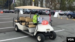 资料照片:在马里兰州在一家社区学院校园开设的大型新冠疫苗接种站的停车场,工作人员驾驶电瓶车接送行走不便的民众。(2021年4月12日)