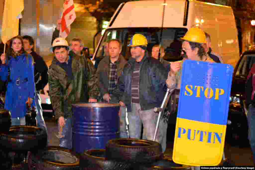 Лісабон. Посольство Росії "Автомобільні шини, металеві бочки, будівельні каски і проливний дощ, дуже правдоподібно відтворили площу Незалежності, символ протистояння проти диктатури. Символ боротьби за ідеали миру і братерства, подвигу простих людей, що силою духу здатні скидати узурпаторів влади", - повідомляє Спілка українців Португалії.