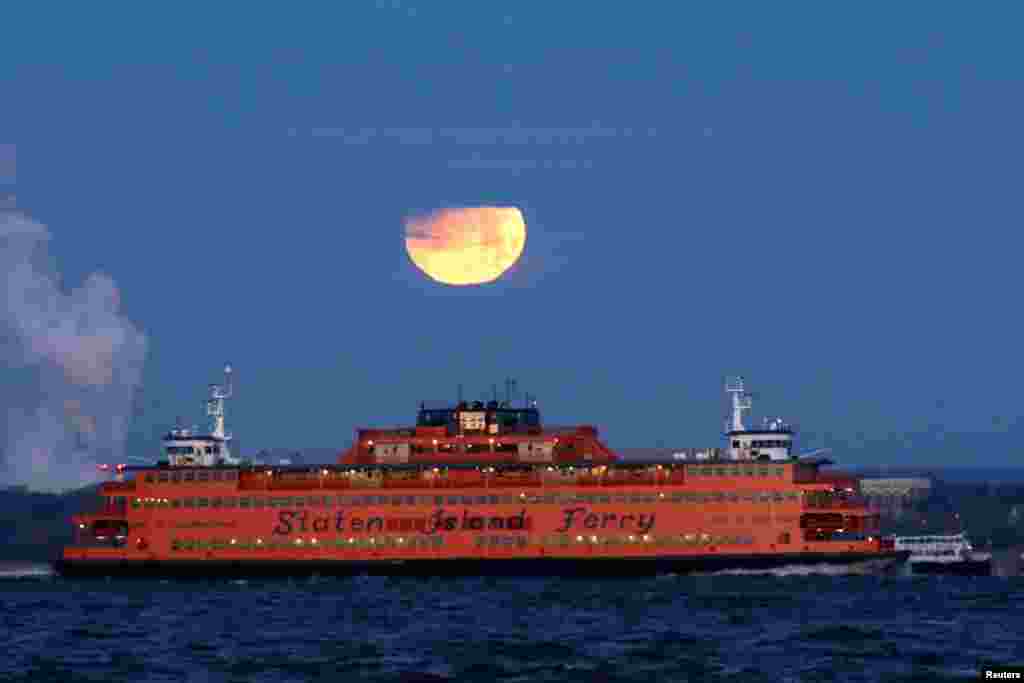 2018年1月31日,在美国纽约布鲁克林眺望史坦顿岛渡口的红黄两色的“超级月”月落。