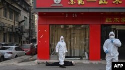 身穿防护服的中国卫生官员在检查一名在武汉一所医院附近倒地死亡的老年男子。(2020年1月30日)