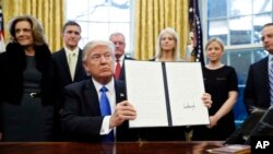 川普总统在白宫椭圆形办公室展示一项签过名的总统行政令。(2017年1月28日)