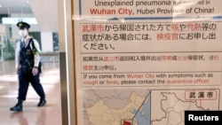 日本东京羽田机场一名戴着口罩的警察走过武汉肺炎的防疫广告牌。（2020年1月20日）