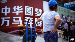 资料照:中国工人在北京一处建筑工地外展示的中国政府宣传“中国梦”的广告牌旁休息。(2016年9月5日)