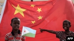 在中国资助的有千所住房单位的吉布提建筑工程启动仪式之前,拿着吉布提国旗的小男孩站在巨大的中国国旗前。(2018年7月4日)