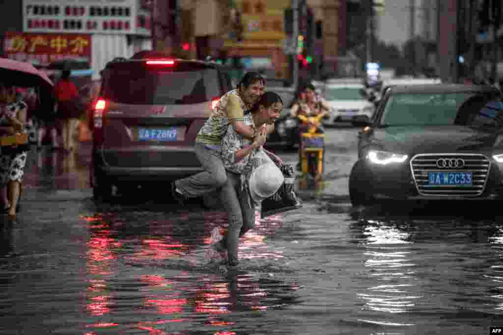 辽宁沈阳,暴雨过后,一位女子背着上了年纪的妇女趟水过街(2017年7月14日) 。近期的媒体报道标题有《沈阳全市陷入暴雨宁山路地面塌陷》《沈阳暴雨袭城,路面坍塌私家车掉深坑》《沈阳遭大风暴雨袭击道路积水严重》