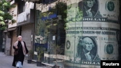 资料照:一位埃及女子走过开罗街头一处张贴着美元广告的外汇兑换处。(2024年5月9日)