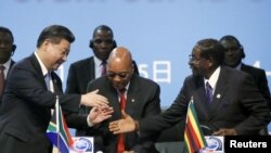 2015年12月4日,中国国家主席习近平在南非约翰内斯堡参加中非合作论坛。图为习近平与津巴布韦总统穆加贝(右边)握手。中间是南非总统祖马。(资料照片)