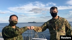 驻日美军司令施耐德(右)与日本自卫队参谋长山崎幸二在日本加贺号护卫舰上见面,背景是美国海军里根号航母。(2020年10月26日)