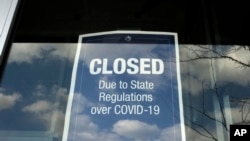 在马萨诸塞州戴德姆的一个露天商场,一家商店的橱窗上贴着一个关闭的告示(2020年4月22日)。