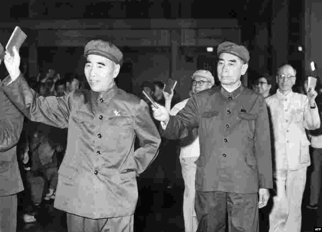 1967年5月,在北京的一次会议上,5位高官列队,举着毛语录。林彪(1907-1971)在前,周恩来(1898-1976)随后,当时的中共第四号人物、中央文革小组组长陈伯达第三,中共第五号人物、中央文革小组顾问康生第四,毛泽东夫人、中央文革小组副组长江青第五,这显示当时她是中共第六号人物,尽管她连中央委员都不是。后来陈伯达被毛泽东打倒,林彪出逃后也被打倒。江青在毛死后被抓,康生在1980年被开除出党,骨灰被“开除”出八宝山。这五个人除了周恩来,都在1980年被列為林彪、江青反革命集团主犯。