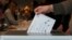 2024年10月8日立陶宛维尔纽斯一名选民在立陶宛大选提前投票期间将选票投入选票箱。