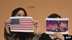 两名香港女子在一个商场内举行的抗议中国人大制定港版国安法的集会上手举美国国旗和川普总统画像。(法新社2020年5月28日)