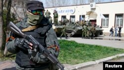 一名戴面罩的亲俄抗议者持枪站立在斯洛文斯克,他的身后是装甲运兵车。(2014年4月16日)