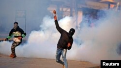 克什米尔地区的一名抗议者冒着印度警察释放的催泪瓦斯投掷石块。（2018年1月13日）