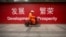 FILE - A maintenance worker rides a scooter past banners reading "Development" and "Prosperity" in English and Chinese on a street in central Beijing, July 15, 2015.