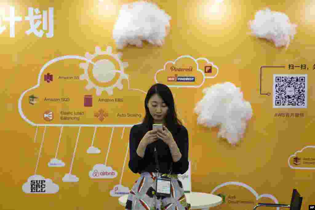 在北京的全球移动互联网大会上,一位女士在推广云服务的摊位前使用手机(2016年4月29日)。这是美国之音2017年4月7日一篇英文报道的封面图片。这篇报道的标题是《进入IT和云计算领域的妇女很少,但这个问题复杂》(Few Women in IT, Cloud Computing, but It’s Complicated)