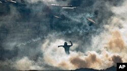 Một người biểu tình chống chính phủ trong thủ đô Caracas của Venezuela, đứng giữa đám khói hơi cay mịt mù, ném đá về hướng Vệ binh Quốc gia, 16/3/14