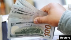 资料照:一人手拿一叠百元美钞。