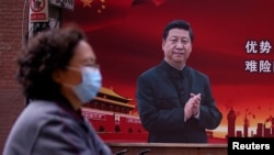 一位戴口罩的妇女从习近平的宣传画前走过(2020年3月12号)。