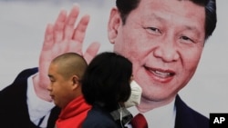 北京街头的习近平大幅照片海报前,有行人走过,有人戴口罩(2017年10月26日)