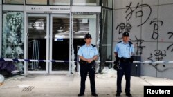 香港警察2019年7月2日站在立法会外被抗议者前一晚示威时涂写在外墙上的涂鸦前。